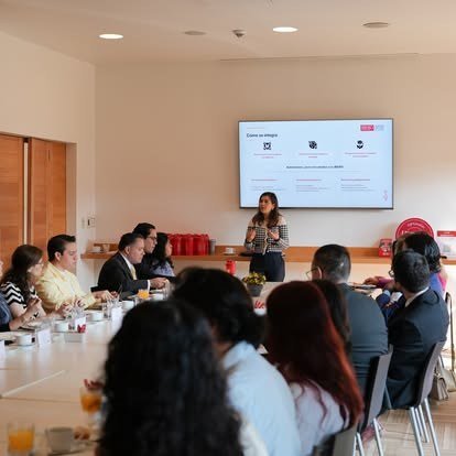 Sala de reuniones con mesas y asistentes frente a una pantalla de presentación