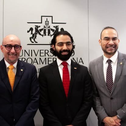 Tres egresados posan frente al escudo de la Universidad Iberoamericana