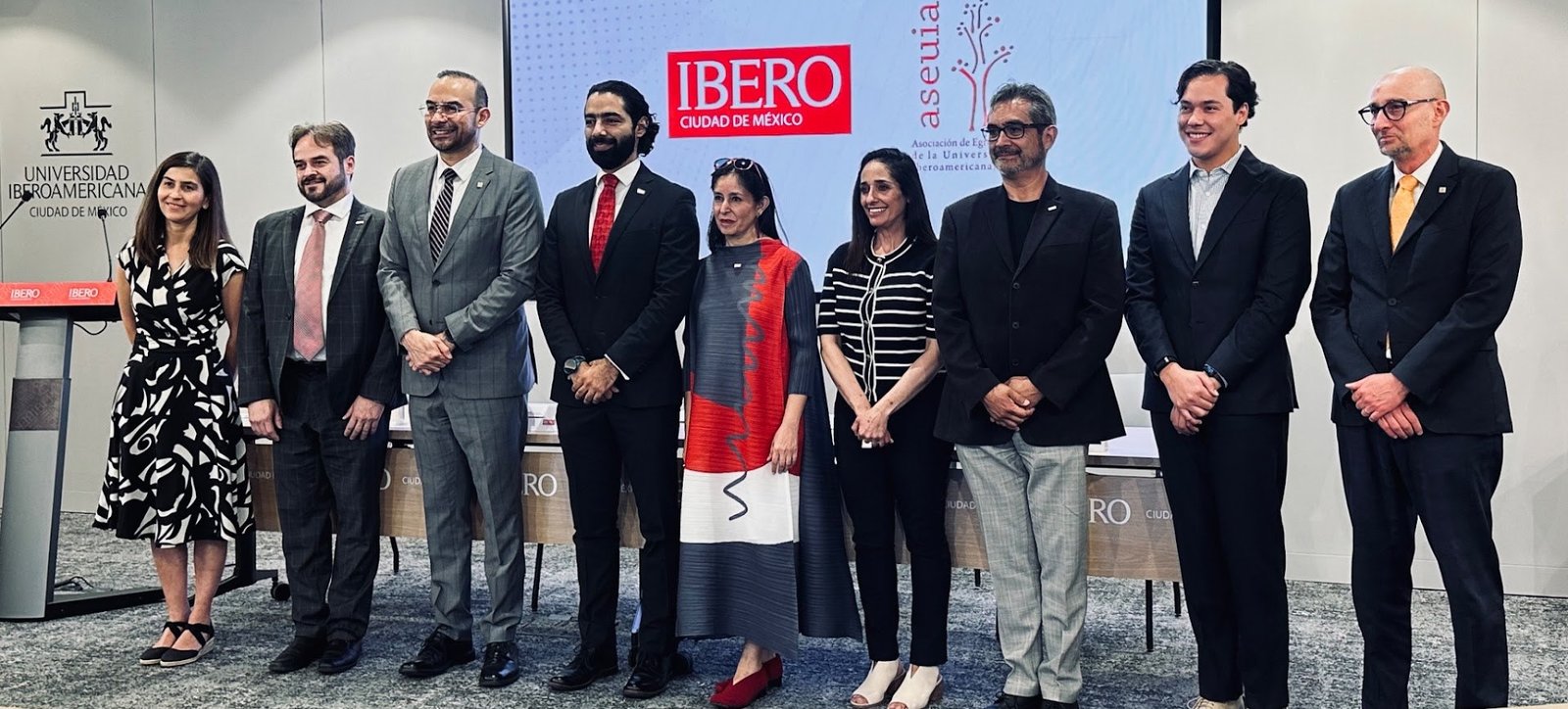 Integrantes de la mesa directiva de ASEUIA de pie frente a una pantalla con los logotipos de IBERO Ciudad de México y aseuia
